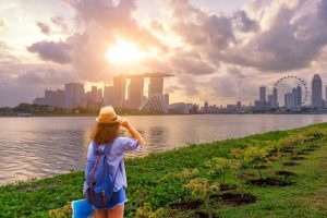 Young woman traveler with sky blue backpack and hat holding the map with singapore city downtown background
